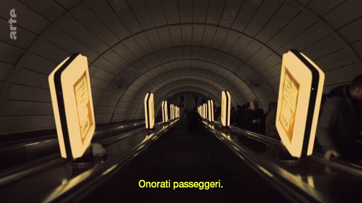 Vue en perspective d'un escalator dans une station de métro souterraine, avec des passagers en arrière-plan et des panneaux publicitaires lumineux le long de la montée. L'image illustre le quotidien des usagers des transports en commun dans un environnement urbain souterrain.
