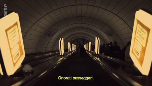 Des passagers descendent dans une station de métro profonde via un escalator, illustrant la vie quotidienne dans les transports souterrains. L'image montre l'architecture typique des stations de métro avec des panneaux publicitaires lumineux le long de la voie.