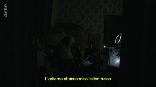 Une personne âgée est assise dans une pièce plongée dans l'obscurité, illustrant les conséquences de l'attaque missilistique russe sur les infrastructures énergétiques. Le sous-titre indique 'L'odierno attacco missilistico russo'.