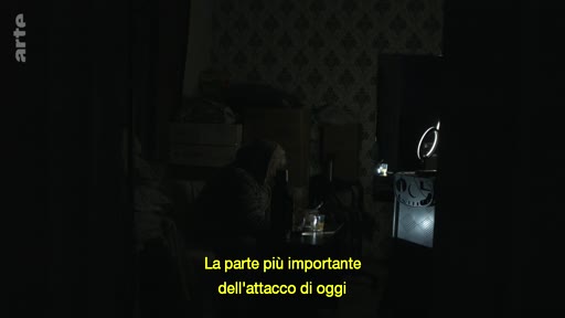 Une vue intérieure sombre d'une pièce avec un sous-titre en italien indiquant 'La parte più importante dell'attacco di oggi', suggérant un contexte de reportage sur un conflit ou une attaque.