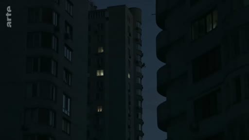 Vue nocturne de façades d'immeubles résidentiels avec quelques fenêtres éclairées, illustrant une ambiance d'isolement urbain.