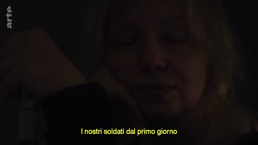 Une femme ukrainienne témoigne dans une pièce sombre, évoquant le rôle des soldats depuis le début du conflit en Ukraine. L'image souligne l'atmosphère tendue et personnelle d'un témoignage sur la guerre.