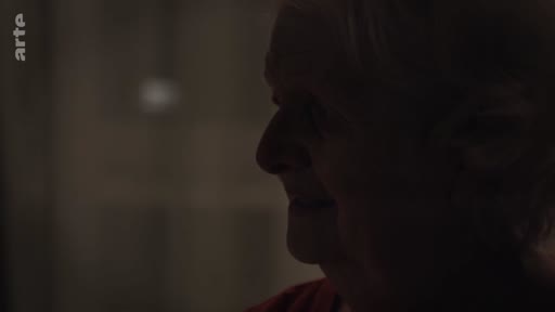 Gros plan sur le visage d'une personne âgée dans une pièce sombre, illustrant le quotidien d'un foyer ukrainien en soirée.