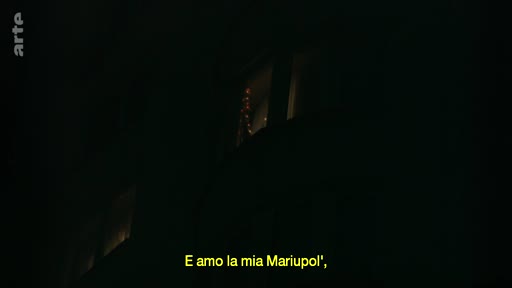 Vue nocturne d'un immeuble résidentiel à Marioupol, accompagnée d'un sous-titre en italien exprimant un attachement à la ville. Cette image illustre le contexte de la guerre en Ukraine et la situation dans la ville de Marioupol.