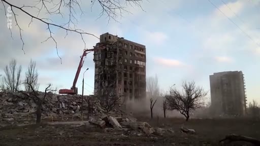 Une pelleteuse de démolition est utilisée pour détruire un immeuble d'habitation gravement endommagé lors des combats à Marioupol, en Ukraine. Cette scène illustre les opérations de nettoyage et de reconstruction urbaine dans les zones dévastées par la guerre.