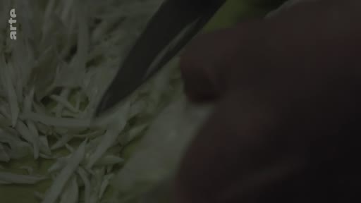 Gros plan sur les mains d'une personne en train d'émincer du chou avec un couteau de cuisine, illustrant la préparation culinaire dans le cadre de la vie quotidienne d'une grand-mère à Londres.