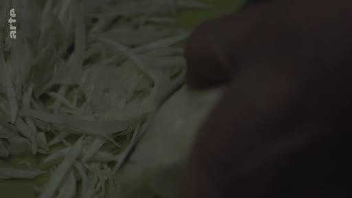 Gros plan sur les mains d'une personne en train d'émincer du chou blanc sur une planche à découper dans une cuisine à Londres.