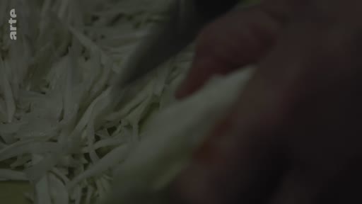 Une personne prépare des légumes en coupant du chou en fines lamelles dans une cuisine, illustrant les tâches quotidiennes d'une grand-mère à Londres.