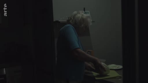 Une femme âgée, vivant à Londres, est filmée dans l'intimité de sa cuisine alors qu'elle prépare à manger. Cette scène illustre le quotidien d'une grand-mère dans la capitale britannique.