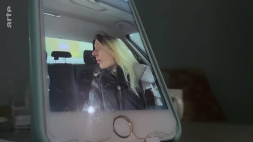 Une jeune femme blonde est filmée en gros plan à travers l'écran d'un smartphone, suggérant un appel vidéo ou un enregistrement personnel dans le cadre d'un reportage sur une vie à Londres.