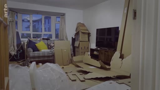 Un salon en désordre rempli de cartons de déménagement et de pièces de meubles en kit, illustrant les difficultés de logement à Londres.