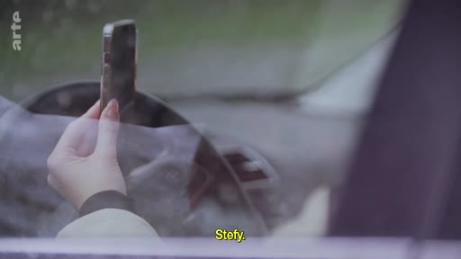 Une main tenant un smartphone à l'intérieur d'un véhicule, illustrant une communication personnelle ou un moment de tension dans le cadre d'un reportage sur le poids psychologique d'un conflit.