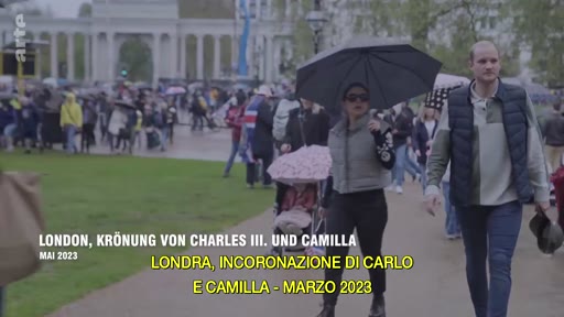 Des personnes marchent dans un parc à Londres lors des préparatifs du couronnement de Charles III et Camilla en mai 2023. Le texte à l'écran indique le contexte de l'événement royal.