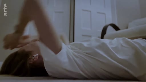 Une personne en t-shirt blanc est allongée sur le sol, les mains posées sur son visage, évoquant un moment de méditation existentielle ou de détresse psychologique.