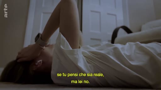 Une personne allongée sur le sol, la main sur le front, dans une posture de réflexion ou de détresse, avec un sous-titre en italien évoquant la réalité.