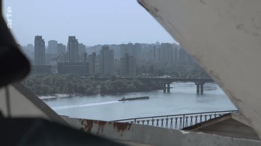 Vue panoramique sur le fleuve Dniepr à Kiev, en Ukraine, montrant un pont traversant le cours d'eau et une barge naviguant sur le fleuve. En arrière-plan, on aperçoit les immeubles résidentiels de la capitale ukrainienne, illustrant le paysage urbain de Kiev.
