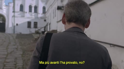 Un homme vu de dos marche dans une ruelle pavée le long d'un bâtiment historique, dans une séquence évoquant des réflexions sur l'amour et l'enfance. Le sous-titre indique : « Ma più avanti l'ha provato, no? ».