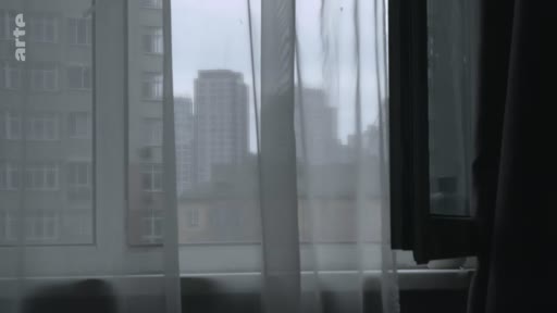 Vue urbaine à travers une fenêtre avec des rideaux, montrant des immeubles résidentiels dans un contexte de vie à Kiev ou Mariupol.