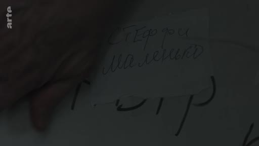 Un gros plan sur un morceau de papier portant des inscriptions manuscrites en cyrillique, probablement liées à des souvenirs de Mariupol ou de la vie en Ukraine.