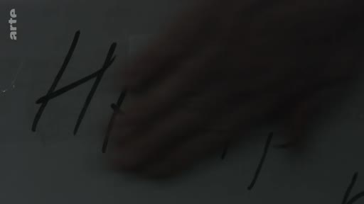 Une main efface une inscription manuscrite sur une vitre, évoquant le souvenir de la ville de Mariupol dans le cadre d'un témoignage sur la vie en Ukraine.