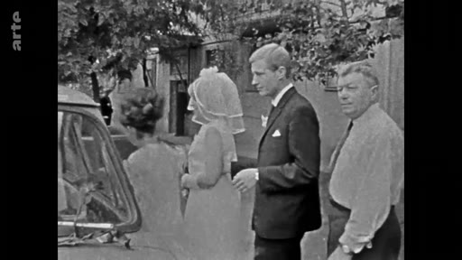 Un jeune couple de mariés, la femme portant une robe blanche et un voile, sort d'une voiture lors d'une cérémonie de mariage en extérieur. Ils sont accompagnés par un homme plus âgé en chemise.