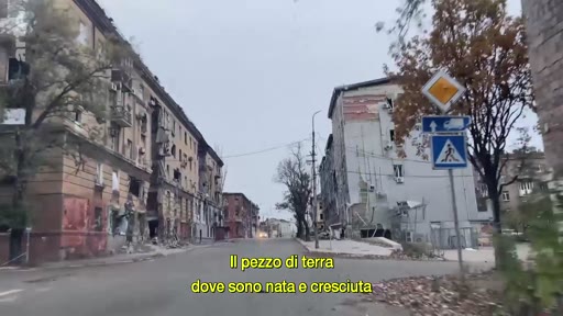 Vue d'une rue bordée d'immeubles résidentiels gravement endommagés par les combats en Ukraine, avec des panneaux de signalisation visibles au premier plan. L'image illustre les conséquences destructrices de la guerre sur les zones urbaines.