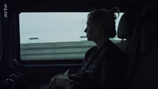 Une femme est assise à l'arrière d'un véhicule, regardant par la fenêtre le paysage qui défile lors d'un trajet, probablement en route vers Londres pour des retrouvailles familiales.