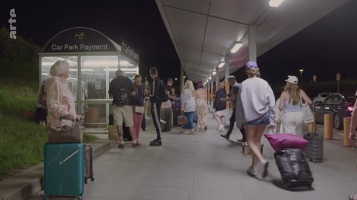 Des voyageurs avec des valises marchent sur le trottoir d'un parking de nuit, près d'une borne de paiement 'Car Park Payment', lors de leur arrivée à Londres.