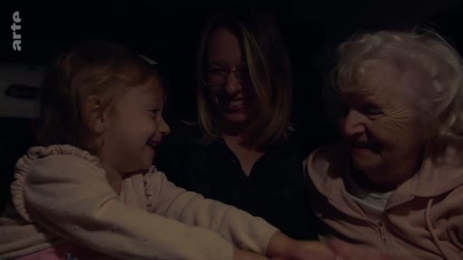 Trois générations de femmes, une petite fille, sa mère et sa grand-mère, sont réunies dans une voiture lors d'un trajet nocturne, illustrant un moment de complicité familiale.