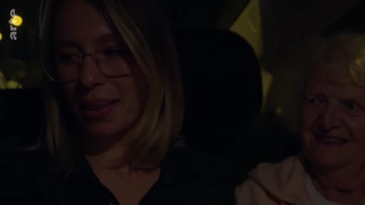 Une jeune femme portant des lunettes et une femme âgée sont assises côte à côte dans une voiture, engagées dans une conversation intime lors d'un trajet nocturne.