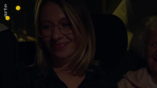 Une jeune femme blonde portant des lunettes sourit lors d'un trajet en voiture de nuit, entourée de membres de sa famille.