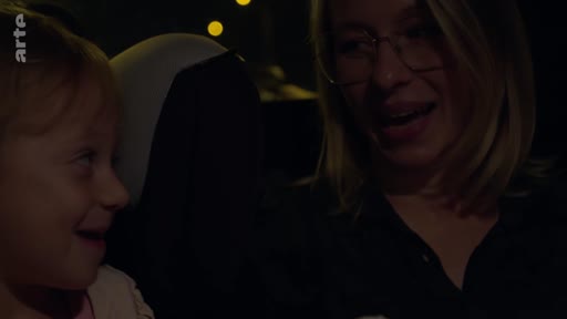 Une femme portant des lunettes discute avec une jeune enfant lors d'un trajet en voiture, dans une ambiance nocturne.