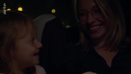 Une femme et une jeune enfant partagent un moment de complicité et sourient à l'intérieur d'une voiture, illustrant une scène de vie familiale.