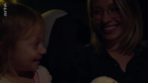 Une femme et une jeune enfant sourient en se regardant à l'intérieur d'une voiture, dans une ambiance intime et chaleureuse. La scène illustre un moment de complicité familiale lors d'un déplacement.
