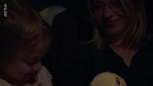 Une femme souriante accompagne une jeune enfant lors d'un trajet en voiture, dans une ambiance intime et nocturne.