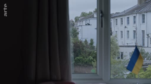 Un petit drapeau de l'Ukraine est visible sur le rebord d'une fenêtre donnant sur des bâtiments résidentiels, symbolisant le soutien au pays dans le contexte du conflit en Ukraine.