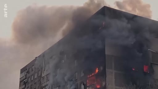 Un immeuble d'habitation en flammes à Kyiv, Ukraine, suite à une attaque militaire. La scène montre les dégâts structurels et la fumée noire s'échappant des étages supérieurs du bâtiment.