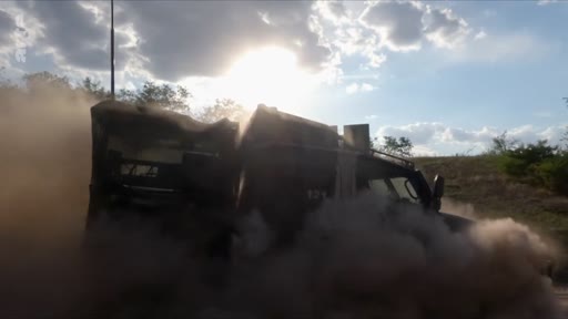 Un véhicule militaire tout-terrain soulève un important nuage de poussière lors d'une progression sur un terrain accidenté, illustrant les conditions de déplacement des troupes en zone de conflit.