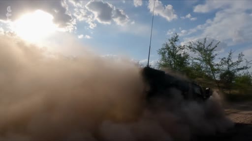 Un véhicule militaire tout-terrain effectue une manœuvre rapide sur un terrain sec, soulevant un épais nuage de poussière sous un ciel ensoleillé. Cette image illustre les conditions de terrain et les déplacements tactiques lors d'opérations militaires.