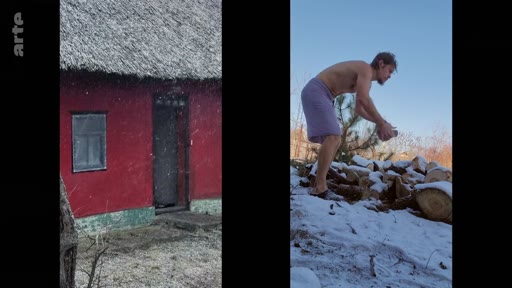 Un homme torse nu, vêtu seulement d'une serviette, ramasse du bois de chauffage dans un environnement enneigé à côté d'une maison traditionnelle aux murs rouges. Cette scène illustre le quotidien rustique et les conditions de vie hivernales dans un village isolé.