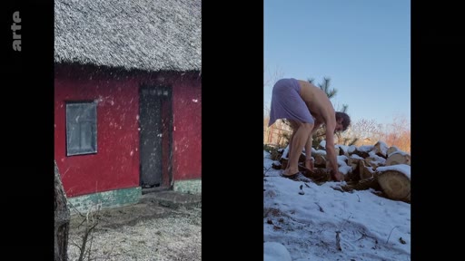 Un homme torse nu ramasse du bois de chauffage dans un environnement enneigé, à côté d'une maison traditionnelle aux murs rouges. Cette scène illustre le mode de vie rustique et la résilience face aux conditions hivernales dans une communauté isolée.