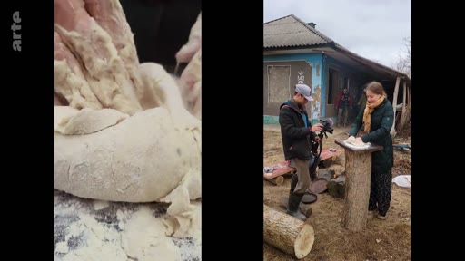Une femme pétrit de la pâte sur un billot de bois en extérieur dans un village, filmée par un caméraman. Cette scène illustre les activités quotidiennes et les traditions culinaires rurales.