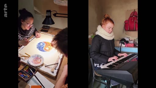Dans un reportage sur la vie en communauté, deux jeunes femmes sont filmées en écran divisé : l'une peint un motif de yin et yang sur une table, tandis que l'autre joue du clavier électronique.