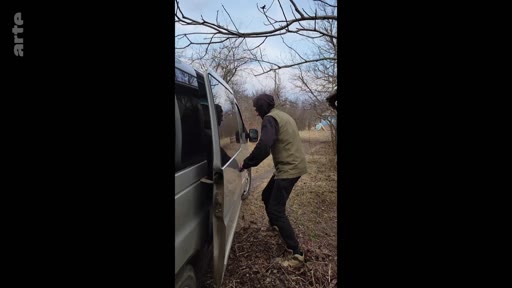 Un homme vêtu d'une veste sans manches et d'un sweat à capuche monte dans un véhicule utilitaire stationné sur un chemin de terre en forêt, dans le cadre d'un reportage sur le départ pour la mobilisation militaire.