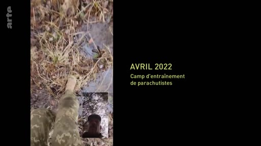 Un soldat en tenue de camouflage filme ses jambes et le sol forestier lors d'un camp d'entraînement de parachutistes en avril 2022. L'image inclut une incrustation vidéo montrant le visage du soldat.
