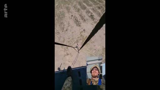 Un soldat ukrainien en tenue de camouflage et casque filme un selfie vidéo depuis l'intérieur d'un hélicoptère en plein vol au-dessus d'un terrain dégagé. Cette séquence illustre le quotidien des forces armées ukrainiennes lors de leurs déplacements aériens.