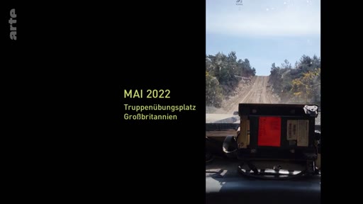 Une vue subjective depuis l'intérieur d'un véhicule militaire circulant sur un terrain d'entraînement au Royaume-Uni en mai 2022. L'image montre le paysage extérieur à travers le pare-brise avec une inscription textuelle précisant la date et le lieu.