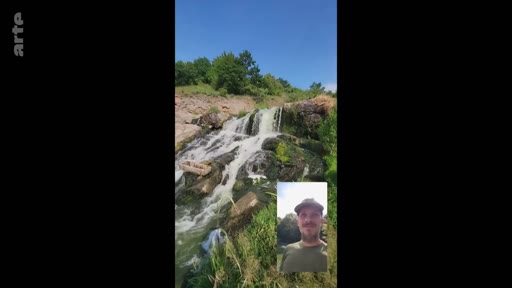 Un homme barbu portant une casquette communique en appel vidéo devant une cascade naturelle en extérieur. L'image montre une vue en incrustation d'un appel en visioconférence sur un paysage de chute d'eau.
