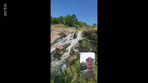 Un homme barbu portant une casquette participe à un appel vidéo en extérieur, avec une cascade en arrière-plan. L'image montre une interaction numérique dans un cadre naturel.