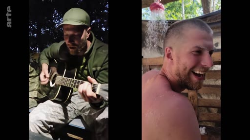 Deux soldats profitent d'un moment de détente dans un campement en forêt, l'un jouant de la guitare acoustique et l'autre se douchant sous une installation rudimentaire.